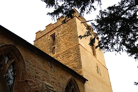A refurbished stone church tower behind the church roof