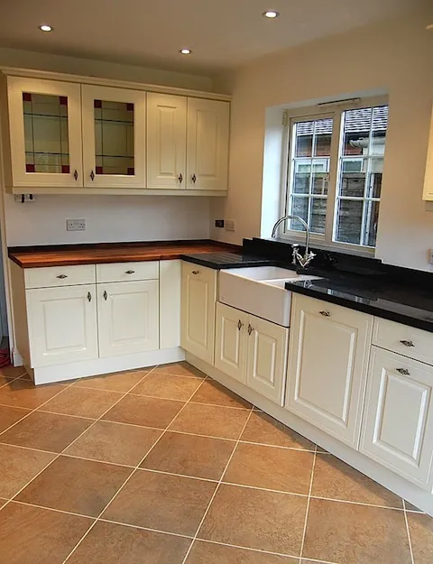 A kitchen with cream units, dark worktops and a tiled floor